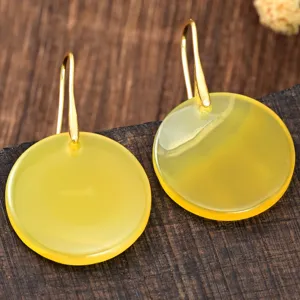 Primer plano detallado de pendientes redondos de ágata amarilla minimalistas con ganchos dorados.
