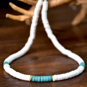 Primo piano dettagliato di una collana di perle heishi bianche con centro turchese e metallo.