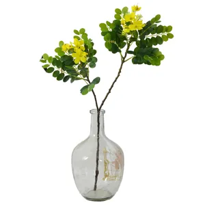 Bouquet de fausses feuilles de fleurs de cassia jaunes dans un vase en verre transparent