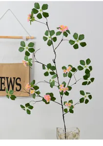 Artificial plant detail with pink flowers, green leaves and branches in a glass vase.
