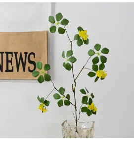 Artificial plant branch with green leaves and yellow flowers in clear glass vase detail shot.