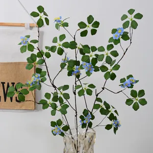 Artificial blue flower branches with green leaves in glass vase for home table decor.