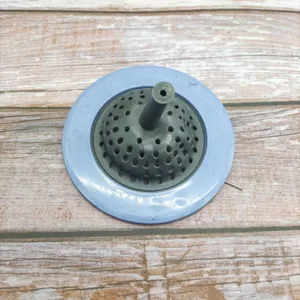 Close-up detail of the grey and blue sink strainer drain cover with central handle and filter holes.