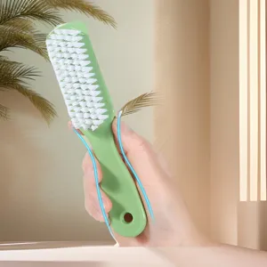 Cepillo de limpieza para zapatos de plástico con cerdas blancas y mango verde duradero.