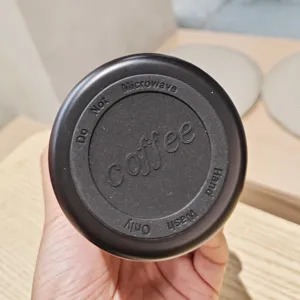 Detailansicht des tragbaren Kaffeetassen-Deckels mit geprägten Produkthinweisen und Warnungen.