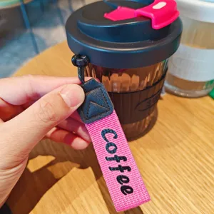 Portable glass coffee cup with heat-resistant sleeve and wrist lanyard for daily office use.