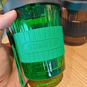 Detail shot of green glass coffee cup with silicone sleeve and portable strap for daily use.