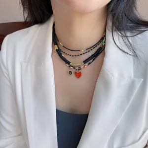 Detailaufnahme einer mehrlagigen schwarzen Perlenkette mit rotem Herzanhänger.