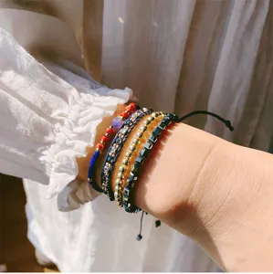 Close-up detail of multi-layer woven bracelet set featuring beads, stones and metal charms.