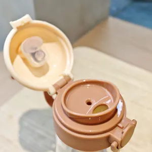 Close-up detail of the portable water bottle pop-up lid and straw mechanism, brown and beige.