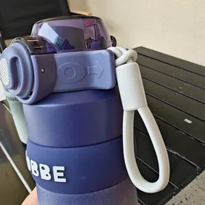 Vista detallada de la botella de agua deportiva, taza morada con tapa y correa blanca.