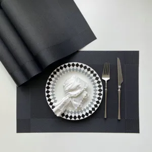 Detailed view of black woven PVC placemat set with elegant tableware on neutral tabletop.