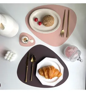 Detail view of irregular PU leather placemats with plates, cutlery and food on table.