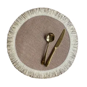 Set da tavola rotondo in juta intrecciata con bordo di frange bianche e posate dorate eleganti.
