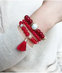 Vista de detalle de pulsera de cuentas rojas multicapa con borla y perla en la muneca.