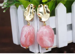 Gros plan detail des boucles d'oreilles longues en resine dore et rose, design elegant.