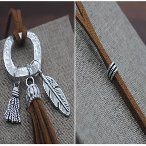 Detalle en primer plano de collar largo de suéter de ante bohemio con colgantes de pluma y borlas.