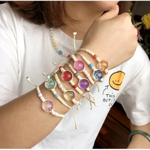 Primo piano di bracciali intrecciati a mano in canapa con fiori secchi e sfere di vetro al polso.