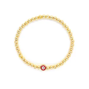 Gros plan d'un bracelet de perles dorées avec un charme rouge en forme d'œil maléfique
