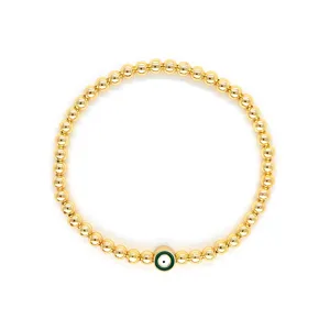 Gros plan d'un bracelet en perles d'or 18 carats avec un œil protecteur vert sur fond blanc.