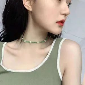 Girocollo choker con perline verdi delicate e fiori bianchi, dettaglio di gioielleria chic.