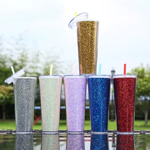 Detailopname van kleurrijke glitterbekers met dubbele wand en rietjes op glazen tafel.