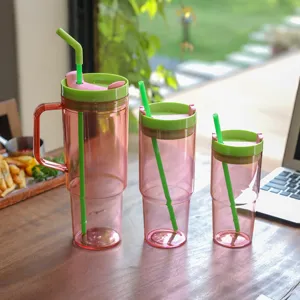 Detail shot of large pink plastic tumblers with green lids and straws in lifestyle setting.