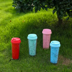Vista detallada de cuatro vasos de plástico con purpurina coloridos en la hierba verde.