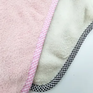 Soft coral fleece towel fabric detail showing dual-color plaid binding edge close-up.