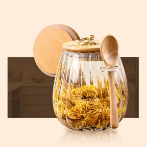 Clear glass storage jar with bamboo lid and wooden spoon for kitchen food pantry use.