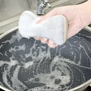 Vue détaillée d'une éponge de nettoyage double face lavant une poêle de cuisine avec de la mousse.