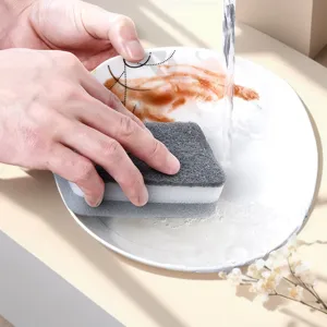Vista detallada de una esponja de cocina de doble cara lavando platos bajo el agua corriente.