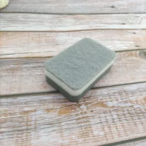 Gros plan d'une éponge de nettoyage double face avec une couche abrasive grise et une mousse blanche.