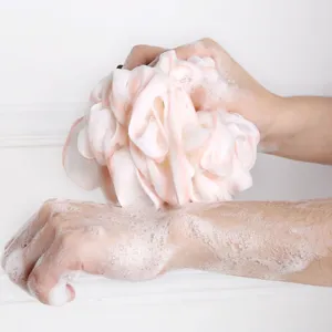 Detail view of large mesh bath sponge pouf creating rich lather for gentle daily shower exfoliation.