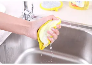 Close-up detail shot of squeezing a yellow dishwashing sponge over a clean kitchen sink.