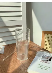 Transparent glass water cup with ribbed design, straw and lid for office and home use.