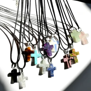 Detailed view of various gemstone cross pendant necklaces with black leather cord for women.