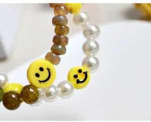 Nahaufnahme des Perlenarmbands mit gelben Smiley-Gesichtern und Rissstein-Perlen.