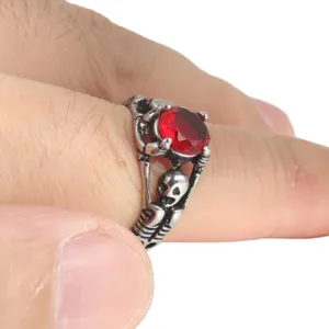 Detalle en primer plano de anillo punk de calavera en acero titanio con gema roja.