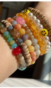 Detailaufnahme von bunten Risssteinperlen und Holzperlen gestapelten Armbändern.