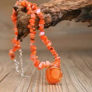 Detailansicht der orangefarbenen Naturstein Splitter Kette mit rundem Anhanger auf Holzbasis.