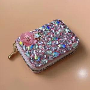 Close-up of a pink zippered card wallet decorated with sparkling rhinestones and a fabric flower.