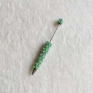Detailed shot of a DIY beaded ballpoint pen adorned with green rhinestones and pearls.