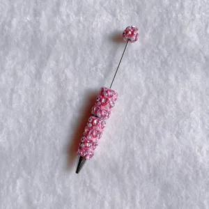 Dettaglio ravvicinato di una penna a sfera decorata con strass rosa e perle scintillanti.