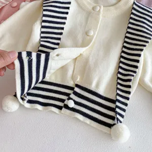 Primer plano de cárdigan de punto para bebé niña, con rayas blanco-negras y pompones bonitos.