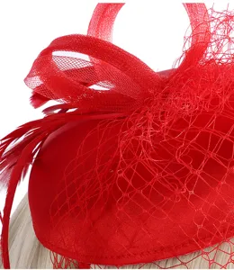 Red fascinator hat close up view, delicate mesh veil and feather bow detail for elegant wedding.