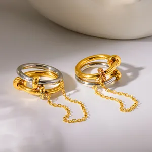 Primer plano de anillos metálicos bicolor con cadenas colgantes y brillantes de estrás.