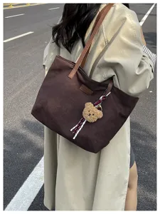 Detail shot of a large brown canvas tote bag with comfortable shoulder straps and cute bear pendant.