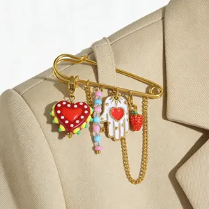 Broche épingle de sûreté en acier plaqué or avec pendentifs cœur et fraise en acrylique.