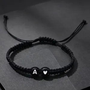 Detail van handgemaakte zwarte gevlochten armband met initiaal letter A en hart bedel.